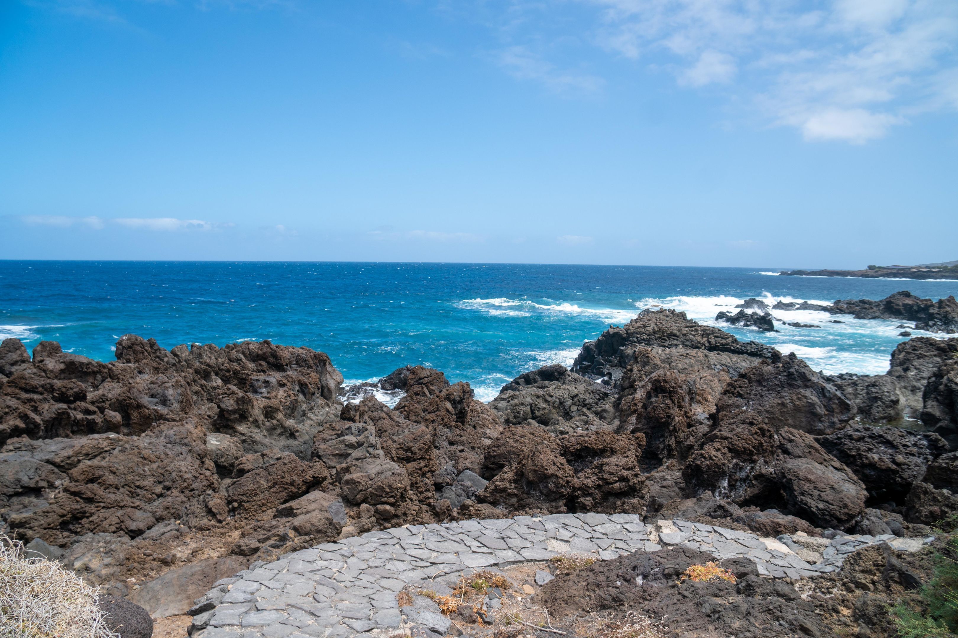 A rocky coastline with the ocean, clear sky, and a paved path.