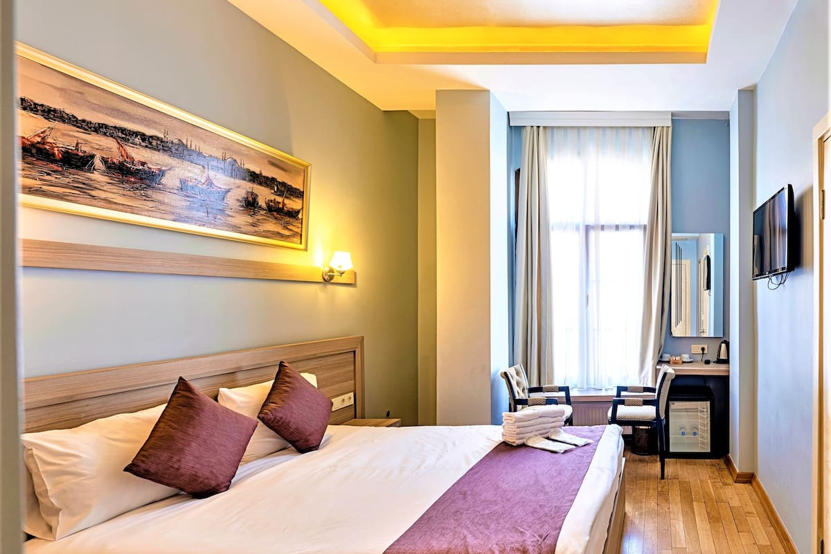 A hotel room with a bed, a desk, a chair, a television, and a painting on the wall.