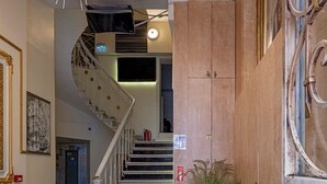 Una escalera de diseño espiral que conduce a un piso superior, una planta grande en maceta y un mueble de madera con pomos ornamentales.