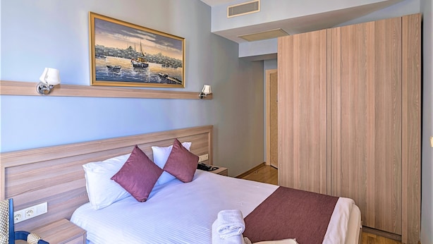 Una habitación de hotel con una cama, una mesita de noche, una lámpara de pared, un cuadro y un armario.