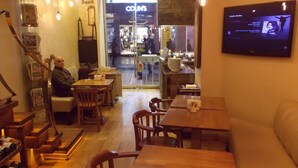 Interior acogedor de restaurante con muebles de madera, un televisor mostrando música y una entrada visible a una tienda llamada 'Colin's'.