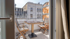 Un balcón con una mesa y dos sillas, vistas a edificios y una puerta con manija.