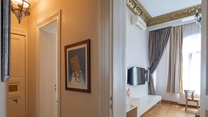 Un pasillo que conduce a un dormitorio con cama, televisor y ventana con cortinas.