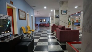 A lobby with a checkered floor, red and yellow chairs, a reception desk, and a gaming console. - Apartamentos Pirámides (Arona)