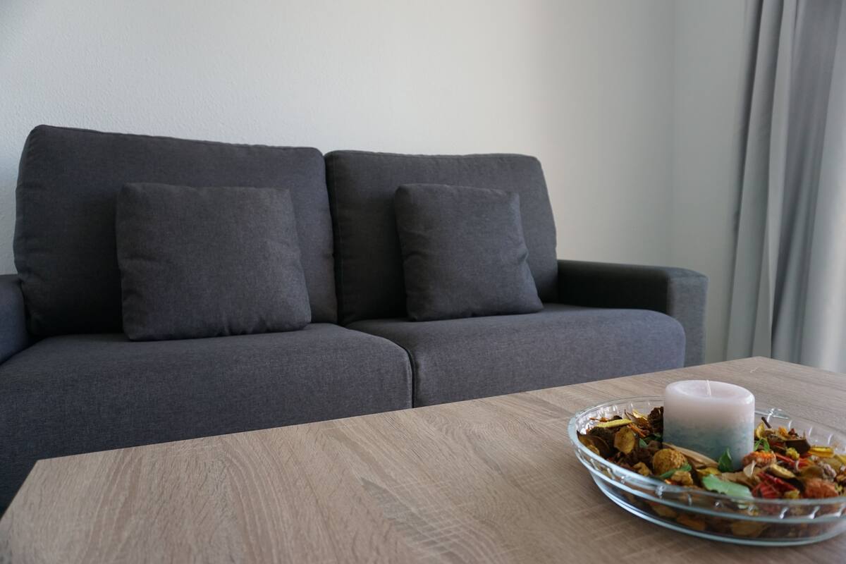 A modern living room with a grey sofa, a wooden coffee table, and a glass bowl with dried flowers and a candle.
