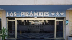 A building entrance with a sign reading "LAS PIRÁMIDES" and a glass door with a checkered floor pattern. - Apartamentos Pirámides (Arona)