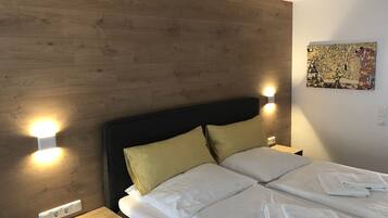 Hotelkamer met houten hoofdeinde, twee bedlampen, een bed met witte lakens en een abstract kunstwerk aan de muur.