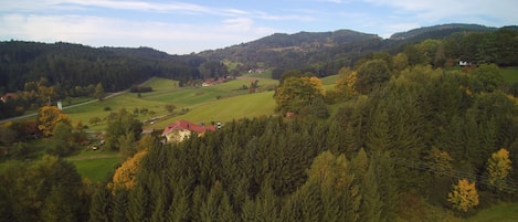 Paisagem rural com colinas onduladas, florestas densas e casas dispersas.