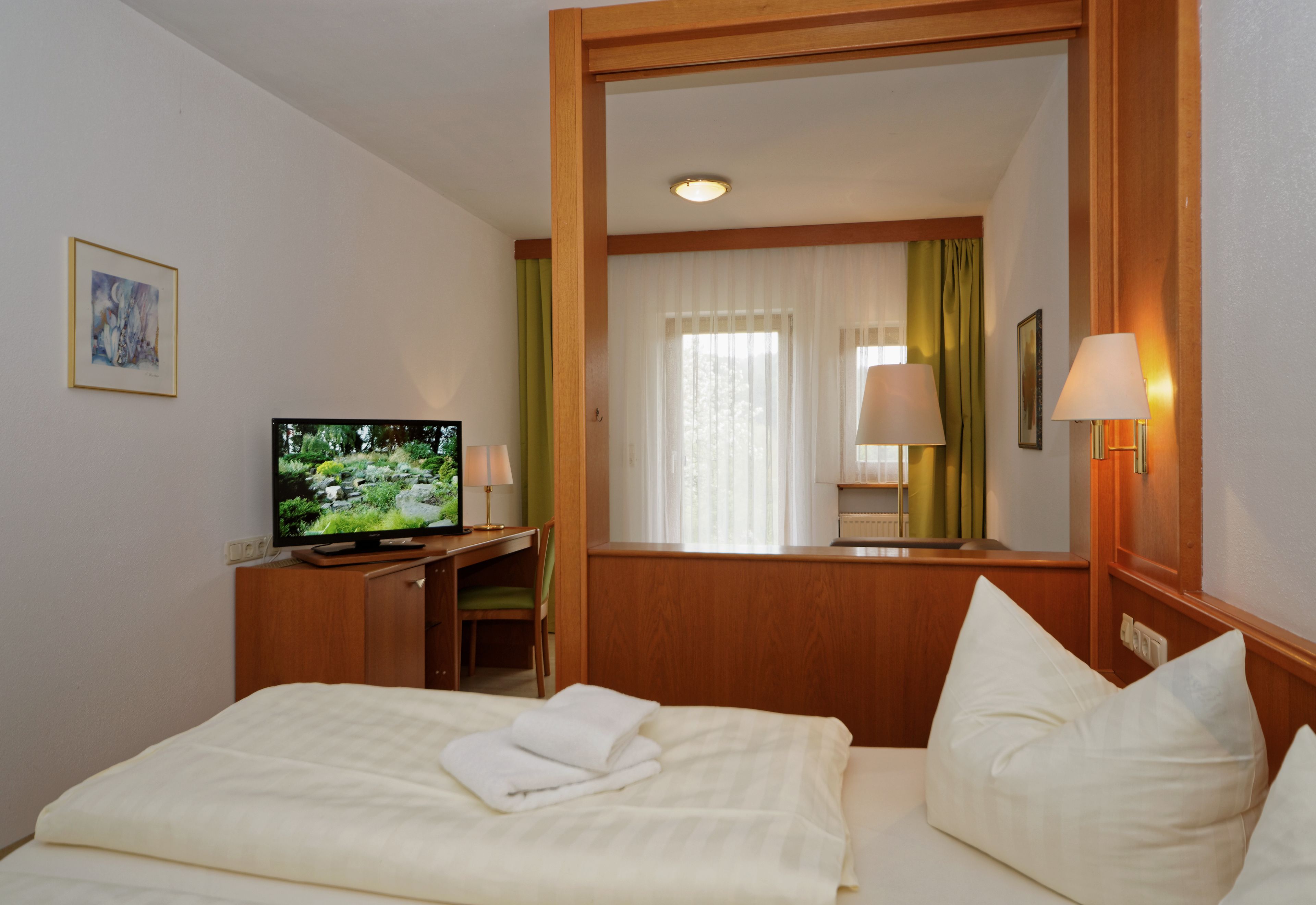 A hotel room with a bed, a desk with a television, a mirror, and a window with curtains.