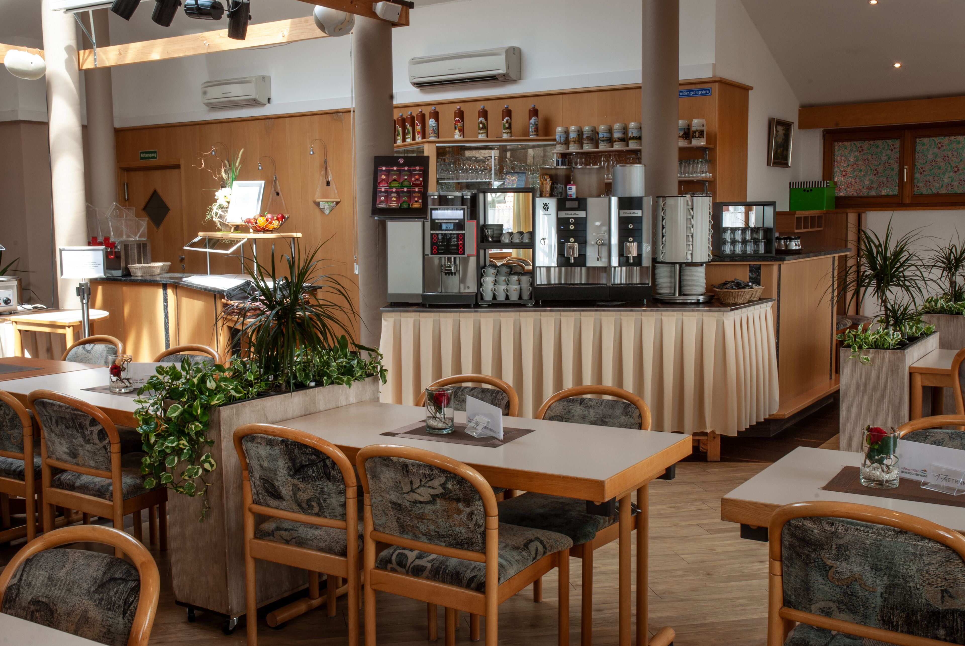 A restaurant with wooden tables and chairs, a coffee bar, and various plants.