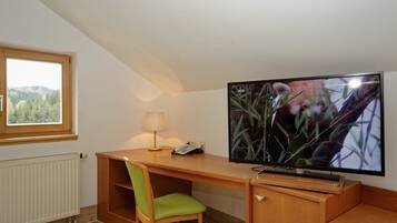 Una habitación con un escritorio de madera, una silla verde, un televisor y una ventana con vistas a un bosque.