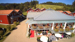 A hotel with multiple red-roofed buildings, a covered outdoor seating area with tables and chairs, and a paved driveway. - Hotel Bayerischer Wald (Neukirchen)