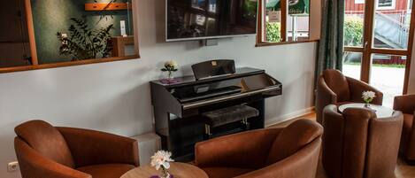 A modern living room with brown leather sofas, a flat-screen TV mounted on the wall, a piano, and a view of a red building outside.