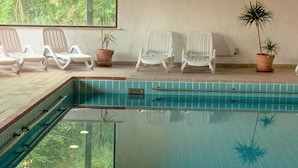 An indoor swimming pool with clear water, surrounded by white lounge chairs and potted plants. - Hotel Bayerischer Wald (Neukirchen)
