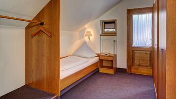 Un dormitorio pequeño y acogedor con una cama nido de madera, una mesita de noche con lámpara, un estante pequeño y una ventana con cortinas.