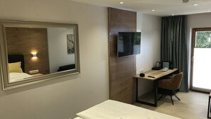 A hotel room with a bed, a desk with a chair, a flat-screen TV, and a large mirror. - Hotel Bayerischer Wald (Neukirchen)