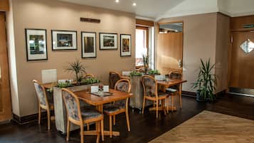 A dining area with wooden tables and chairs, framed pictures on the wall, and potted plants.