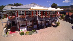 A two-story building with a glass facade, outdoor seating, and flower boxes on the balconies. - Hotel Bayerischer Wald (Neukirchen)