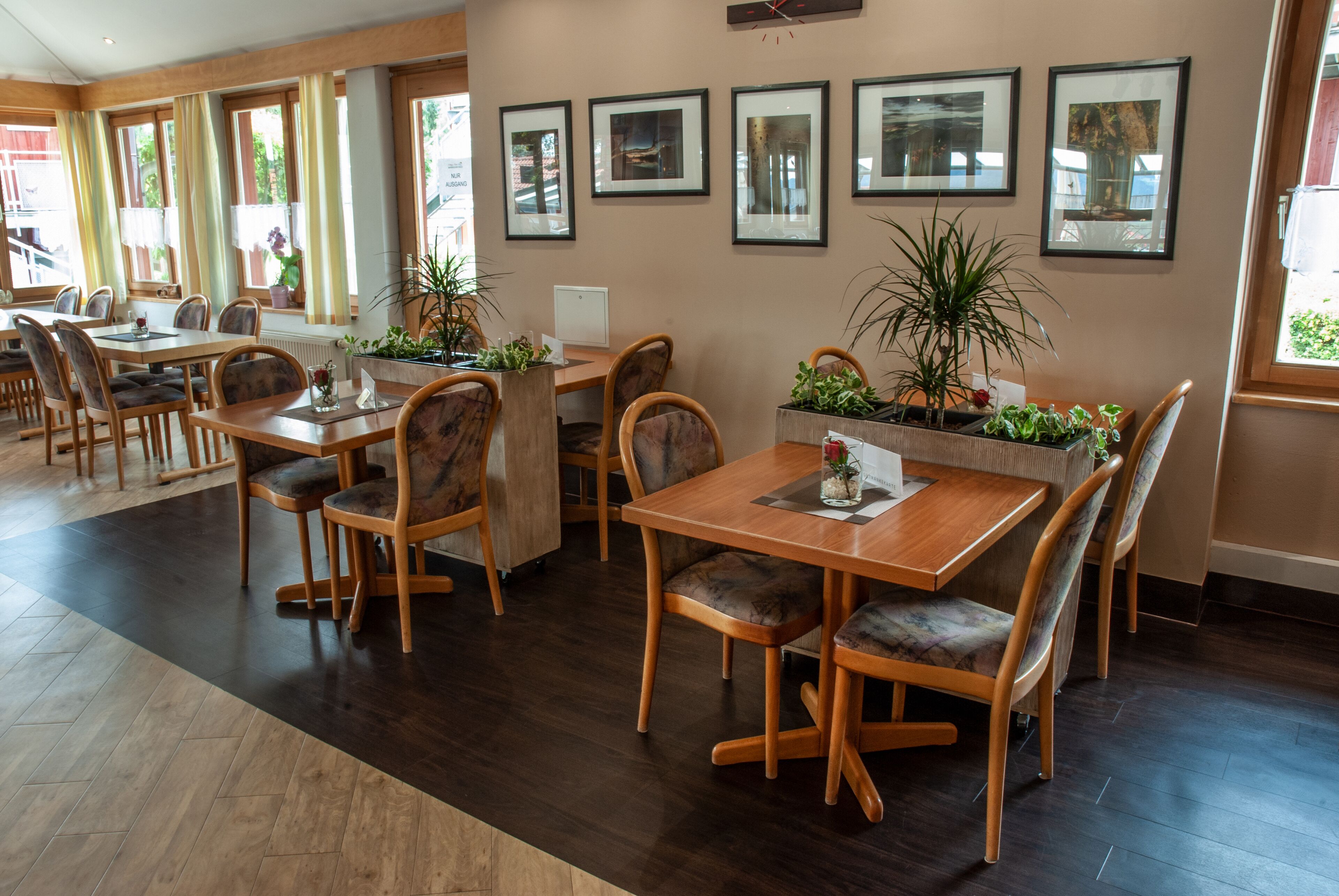 Un vaste espace dédié à la salle à manger, avec des tables et des chaises en bois, des plantes en pot et des œuvres d’art encadrées accrochées aux murs.