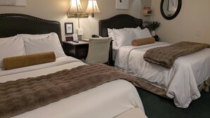 Habitació d'hotel amb dos llits, un escriptori, una cadira, una làmpada i un rellotge.