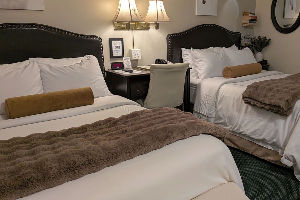 Une chambre d’hôtel avec deux lits, un bureau, une chaise, une lampe et une horloge.