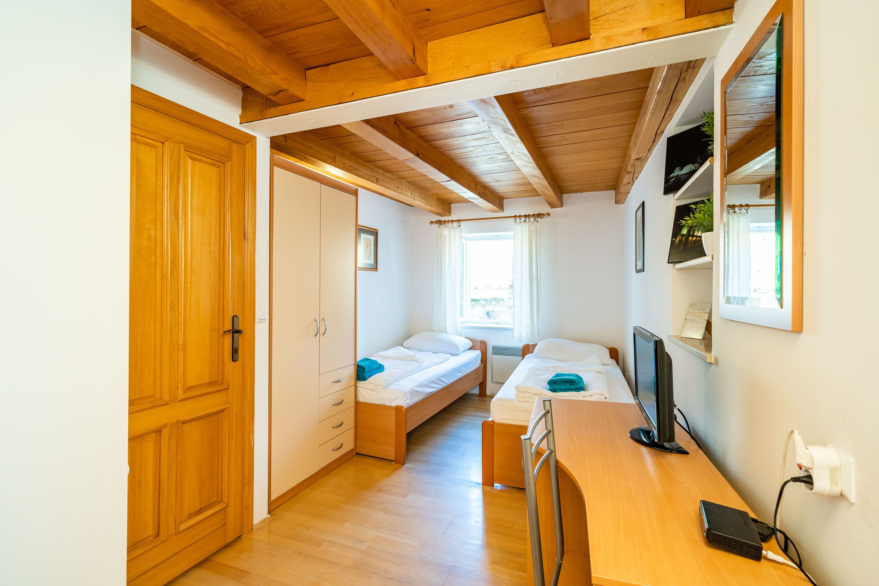 A compact room with two single beds, a wooden desk with a computer, and a large mirror.