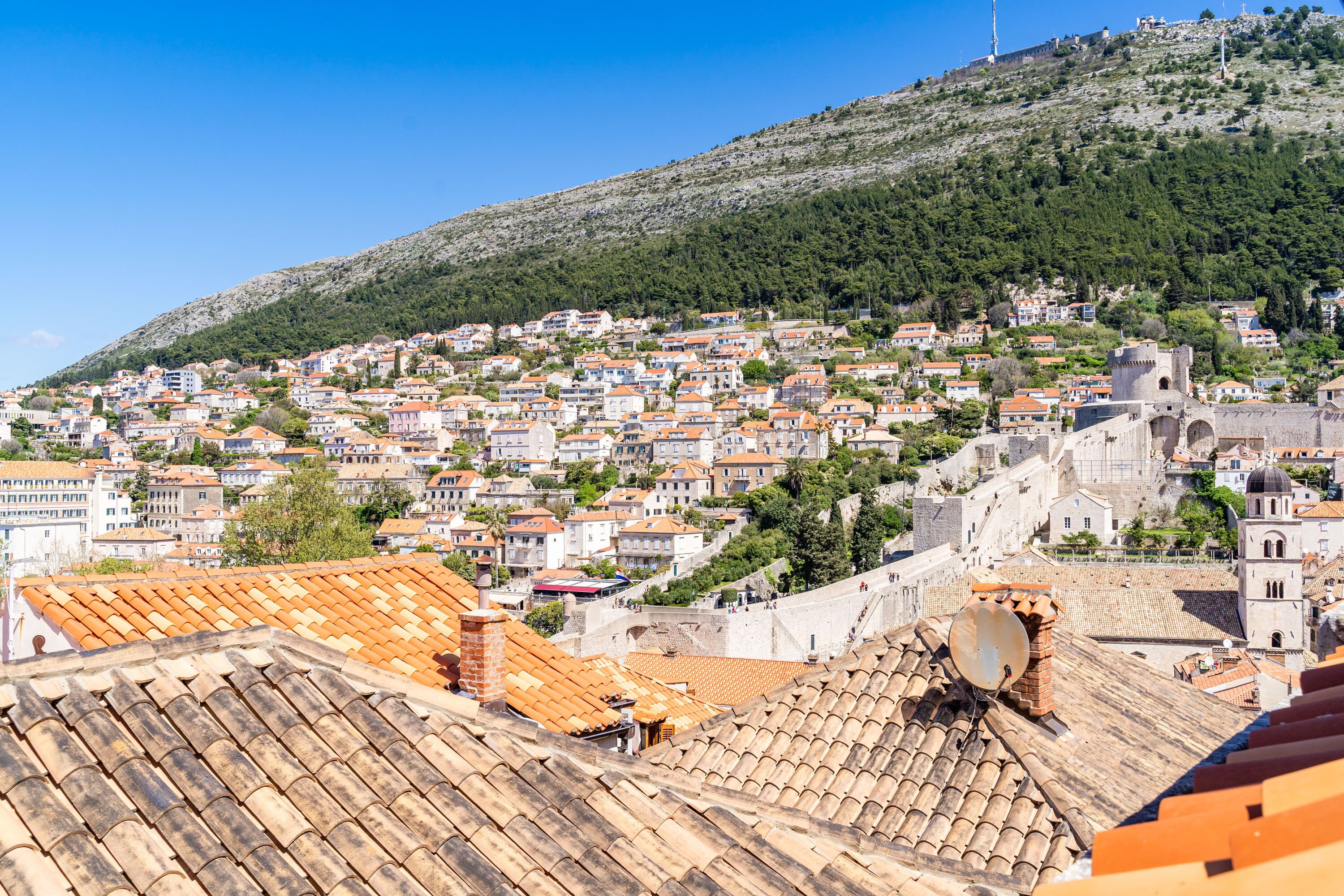 A hillside town with terracotta-roofed buildings, a prominent tower, and a clear blue sky.