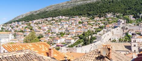 A hillside town with terracotta-roofed buildings, a prominent tower, and a clear blue sky.