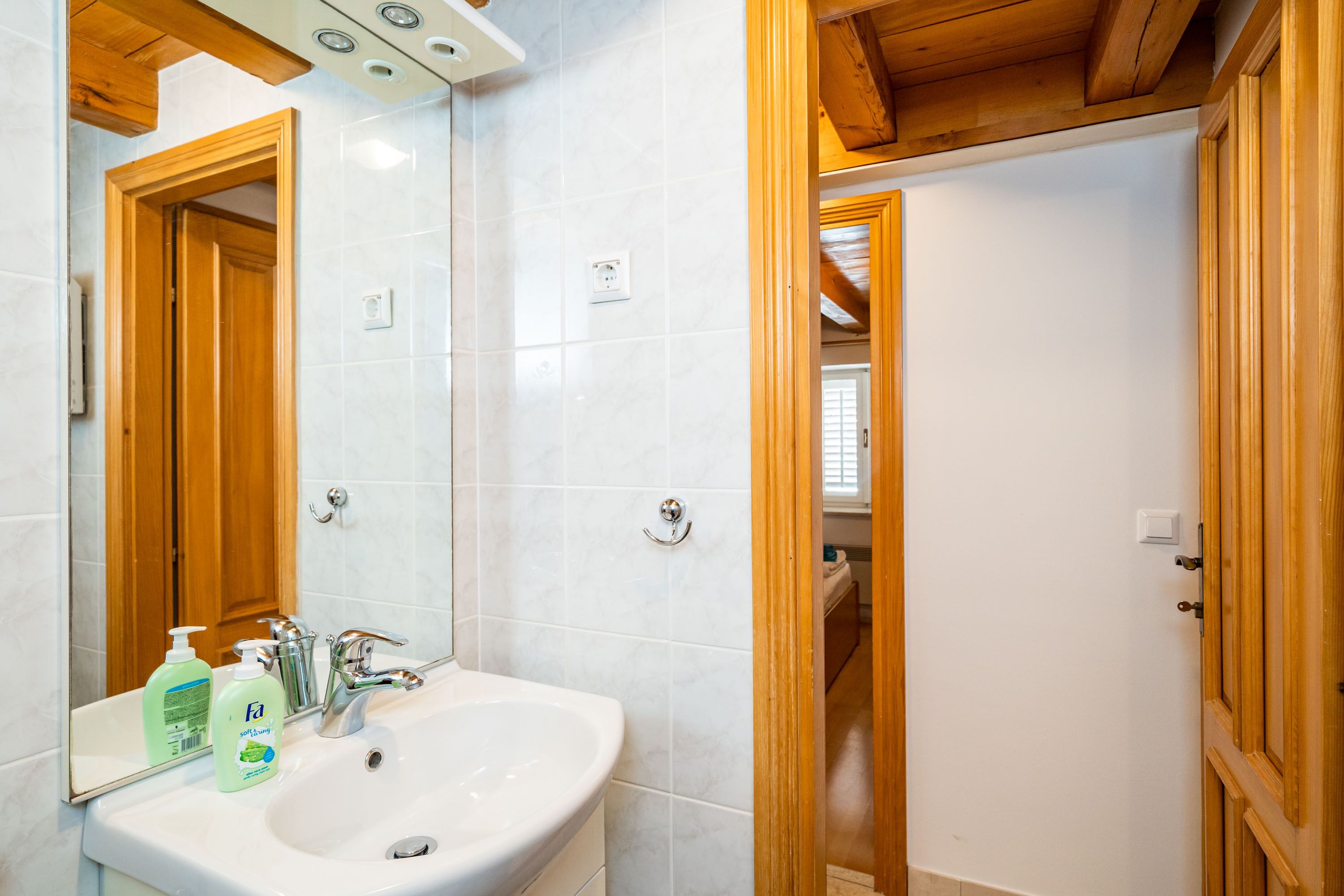 Un baño con un lavabo blanco, una puerta de madera y un espejo.