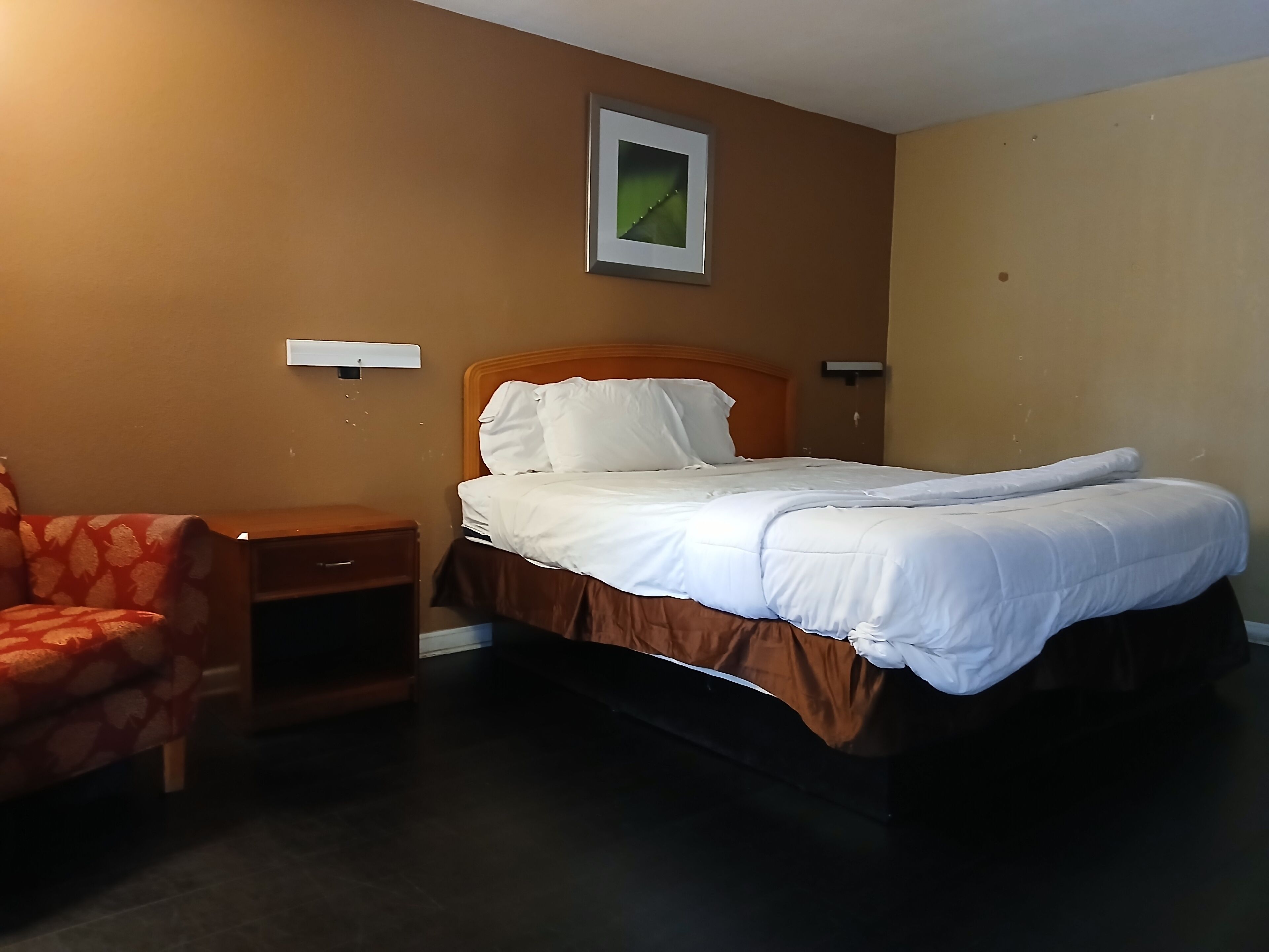 Une chambre d’hôtel avec un lit simple, une table de chevet, une chaise et un tableau accroché au mur.