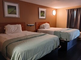 Habitación de hotel con dos camas, una mesita de noche, una lámpara de pared y dos cuadros enmarcados.