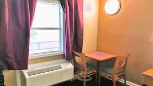 A room with a window, purple curtains, a table with two chairs, and a wall-mounted round mirror. - OYO Hotel Tallahassee Downtown (Tallahassee)