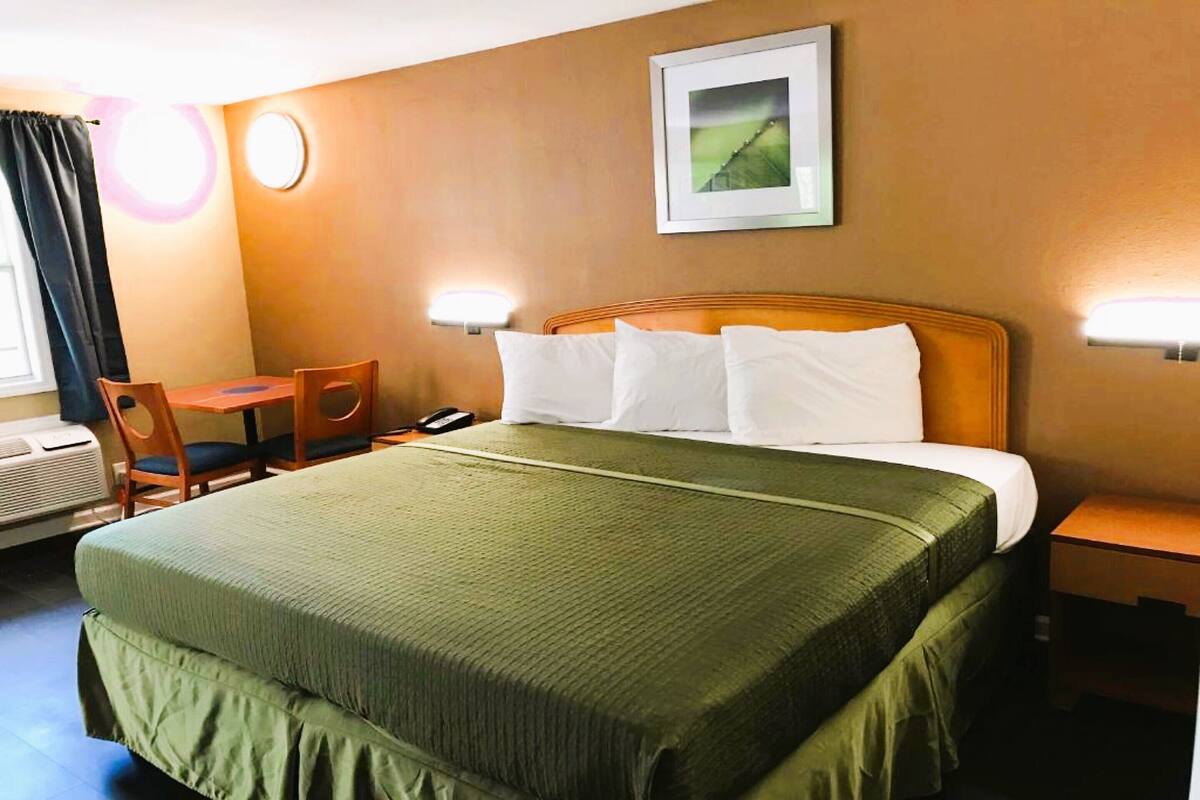 A hotel room with a large bed, a desk with a chair, a phone, and two wall-mounted lamps.