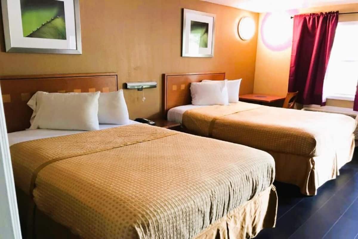 A hotel room with two beds, a nightstand, a lamp, and a window with curtains.