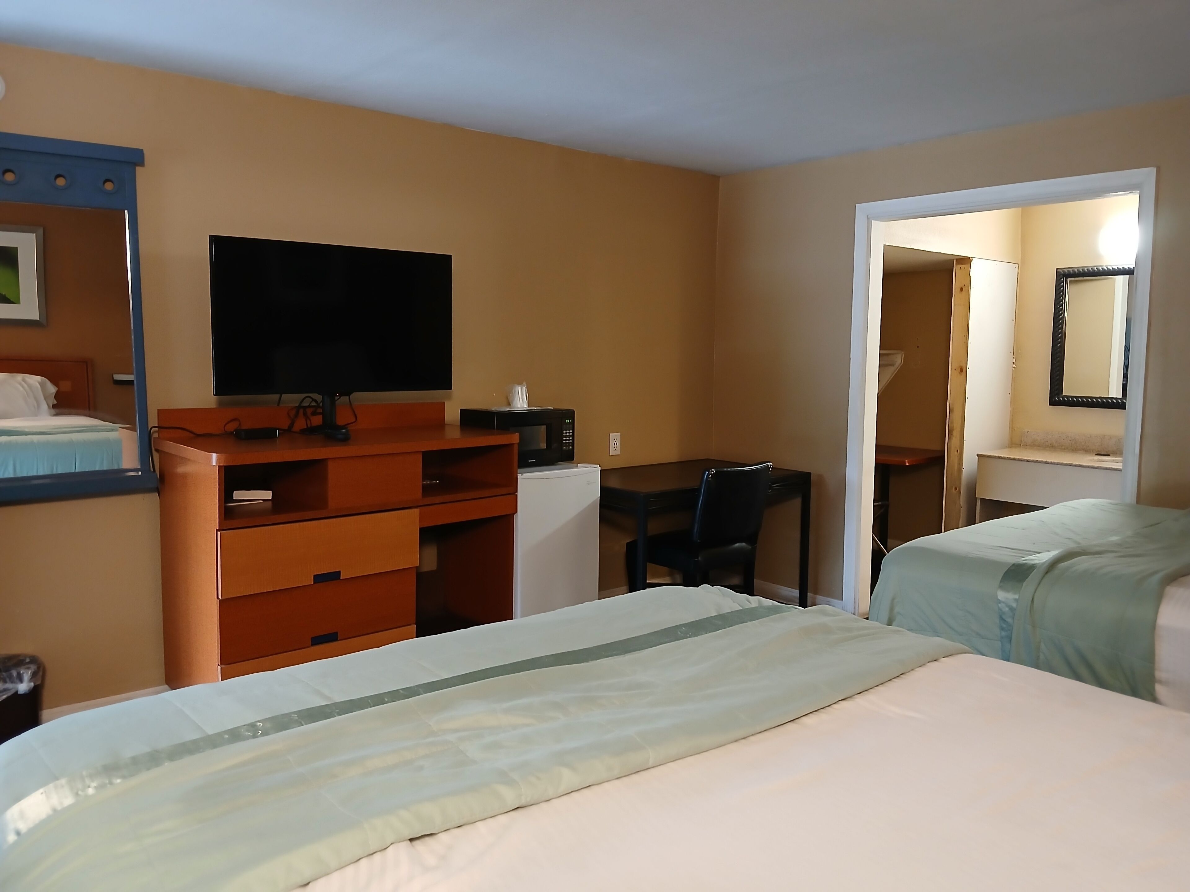 A hotel room with a bed, a desk, a chair, a television, and a microwave.