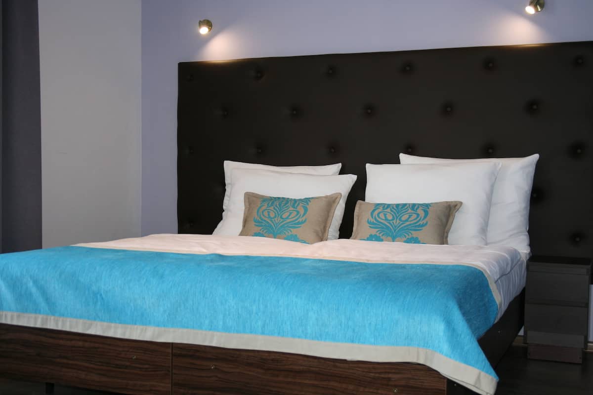 Una cama bien hecha con un cabecero oscuro, almohadas blancas y estampadas, y una colcha azul.