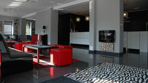 A modern lobby with red seating, a reception desk, and a wall-mounted television. - Hotel Opera (Tarnowskie Gory)