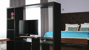 A hotel room with a large TV on a black entertainment unit, a bed with blue bedding, and a wooden headboard. - Hotel Opera (Tarnowskie Gory)