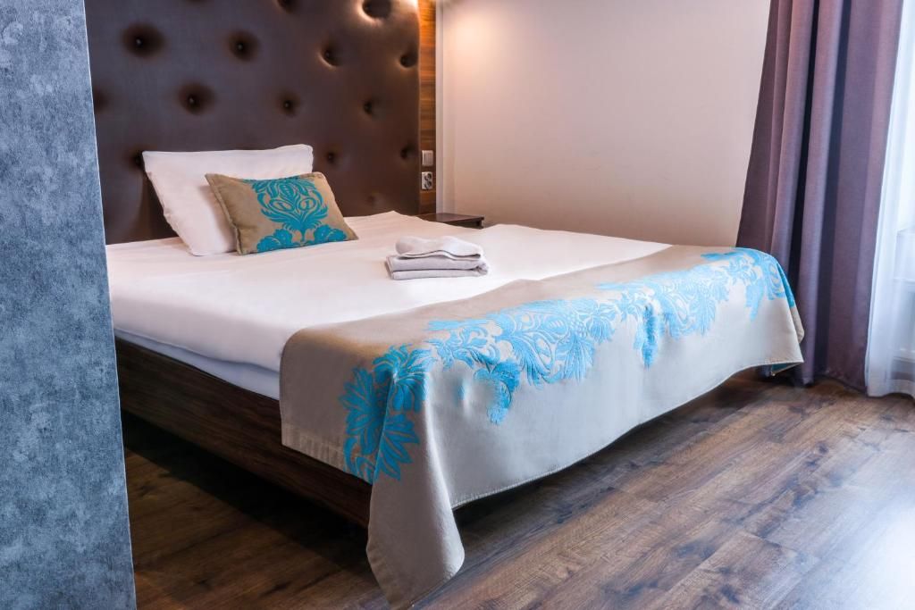 A neatly made bed with a white and blue patterned bedspread, a tufted headboard, and a wooden floor.