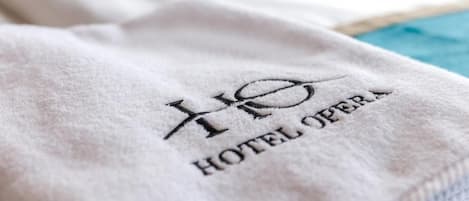 Una toalla blanca con el bordado 'HOTEL OPERA' en negro.