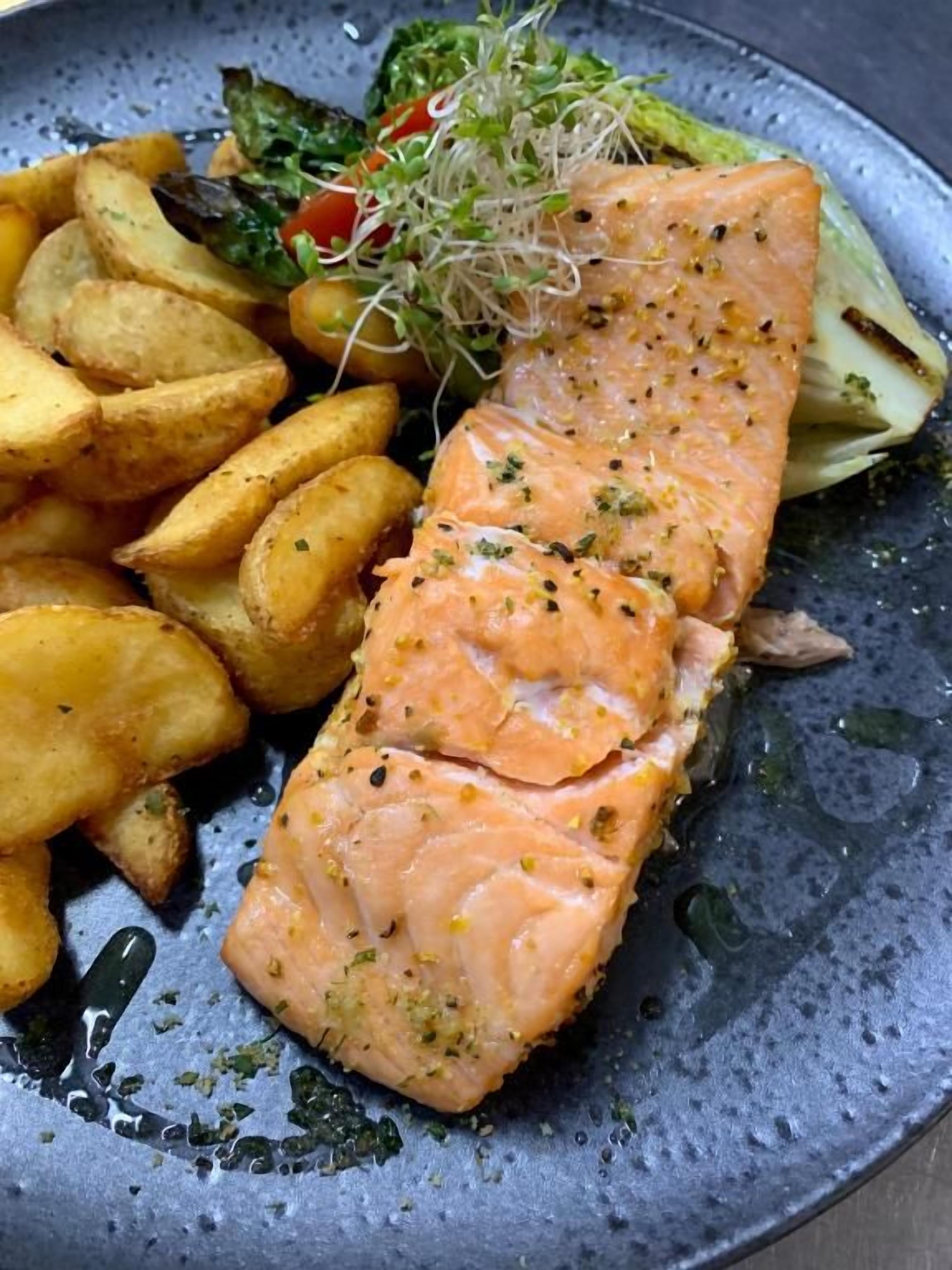 A plate with a piece of salmon, roasted potatoes, and a side salad.