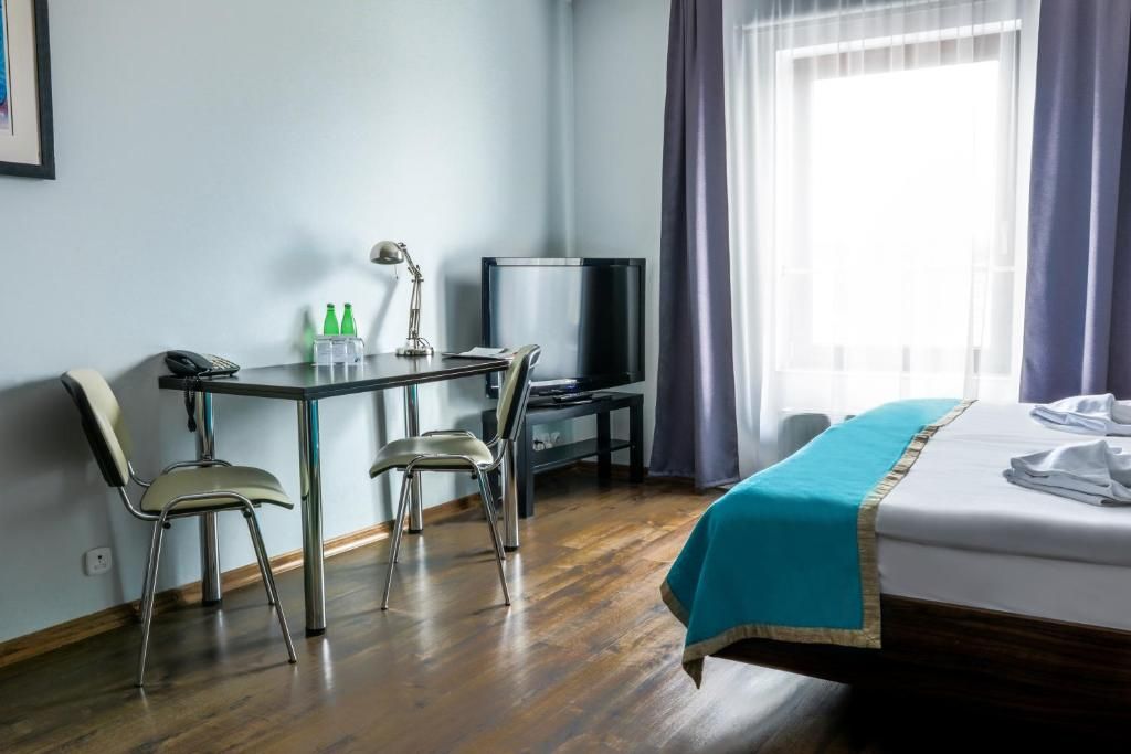 Une chambre d’hôtel avec un lit, un bureau et une chaise, une télévision et une fenêtre avec des rideaux.