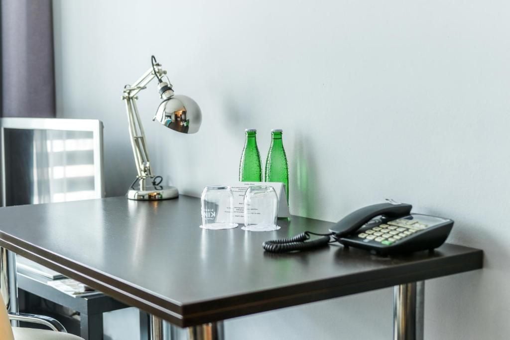 A desk with a desk lamp, two green bottles, a telephone, and a glass.