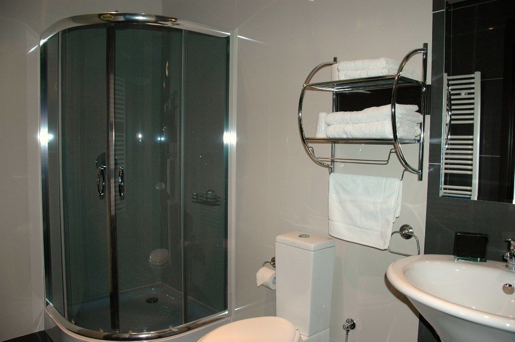A modern bathroom with a glass-enclosed shower, a white toilet, a sink with a mirror, and a towel rack with multiple towels.