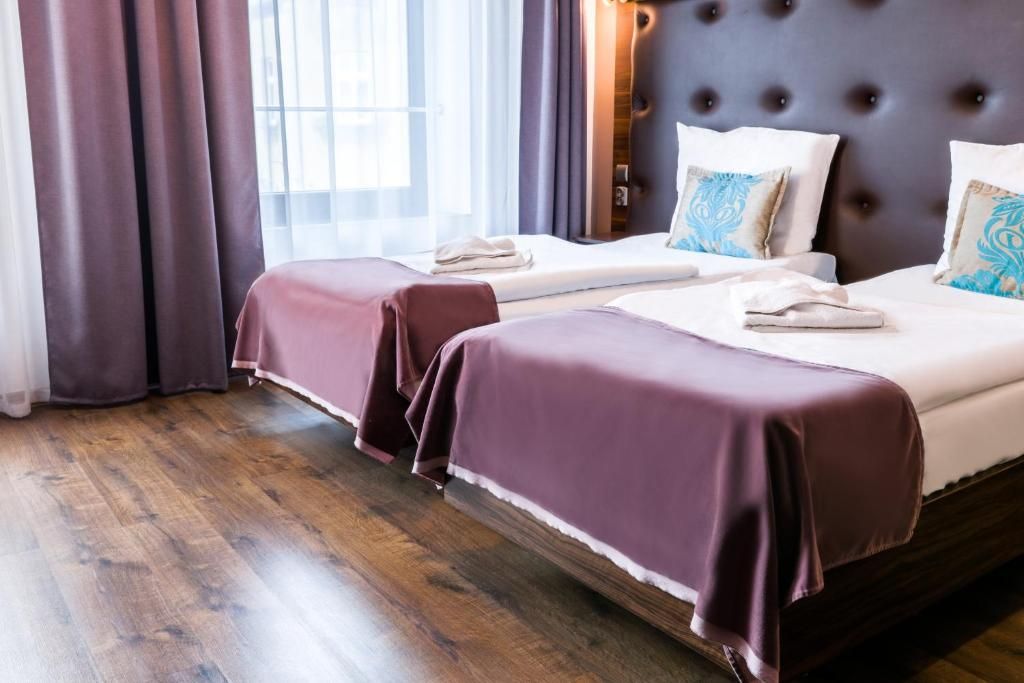 A hotel room with two beds, a dark headboard, and a window with curtains.