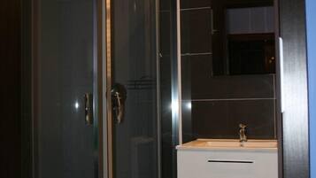 Un baño moderno con ducha envuelta en vidrio, un lavamanos blanco y paredes de azulejos oscuros.