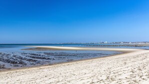 A beach with clear blue water, sandy shore, and a distant pier. - East Harbour Motel and Cottages (North Truro)