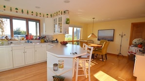 A kitchen with white cabinets, a dining area with a table and chairs, and a large window providing natural light. - East Harbour Motel and Cottages (North Truro)