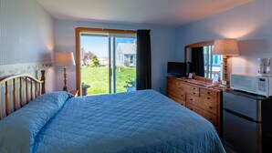 A bedroom with a large bed, a dresser, a television, a microwave, and a sliding glass door leading to a balcony. - East Harbour Motel and Cottages (North Truro)