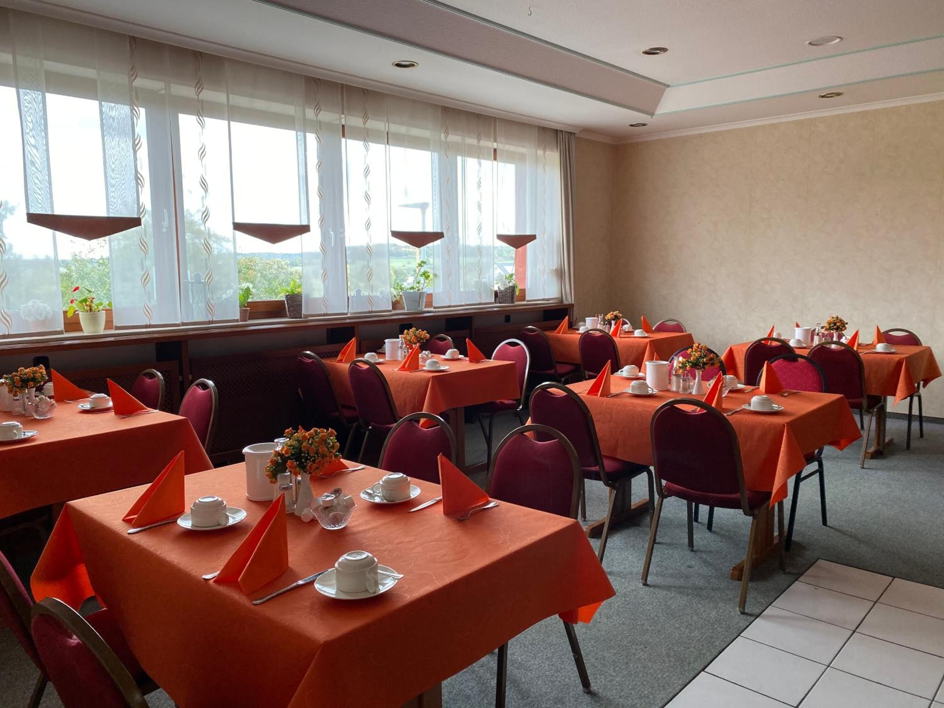 A dining area with multiple tables set for service, each with a tablecloth, chairs, and table settings.